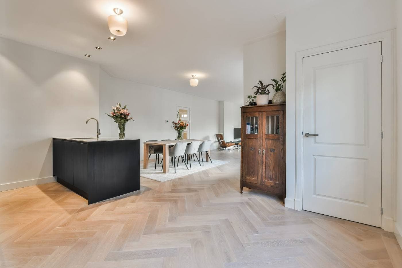 Lyst køkkenalrum med sildebensparket, sort køkkenø og spisebord