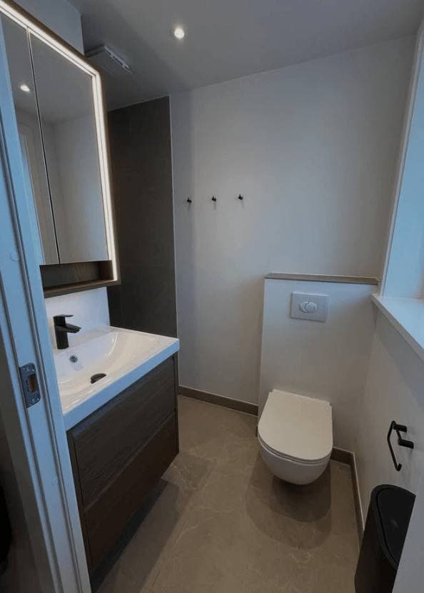 Badeværelse med væghængt toilet og mørkt underskab, udført af RahByg