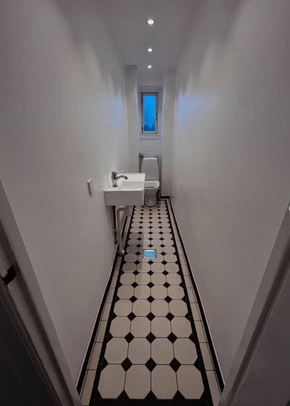 Smalt gæstetoilet med sort og hvidt klinkegulv, udført af RahByg