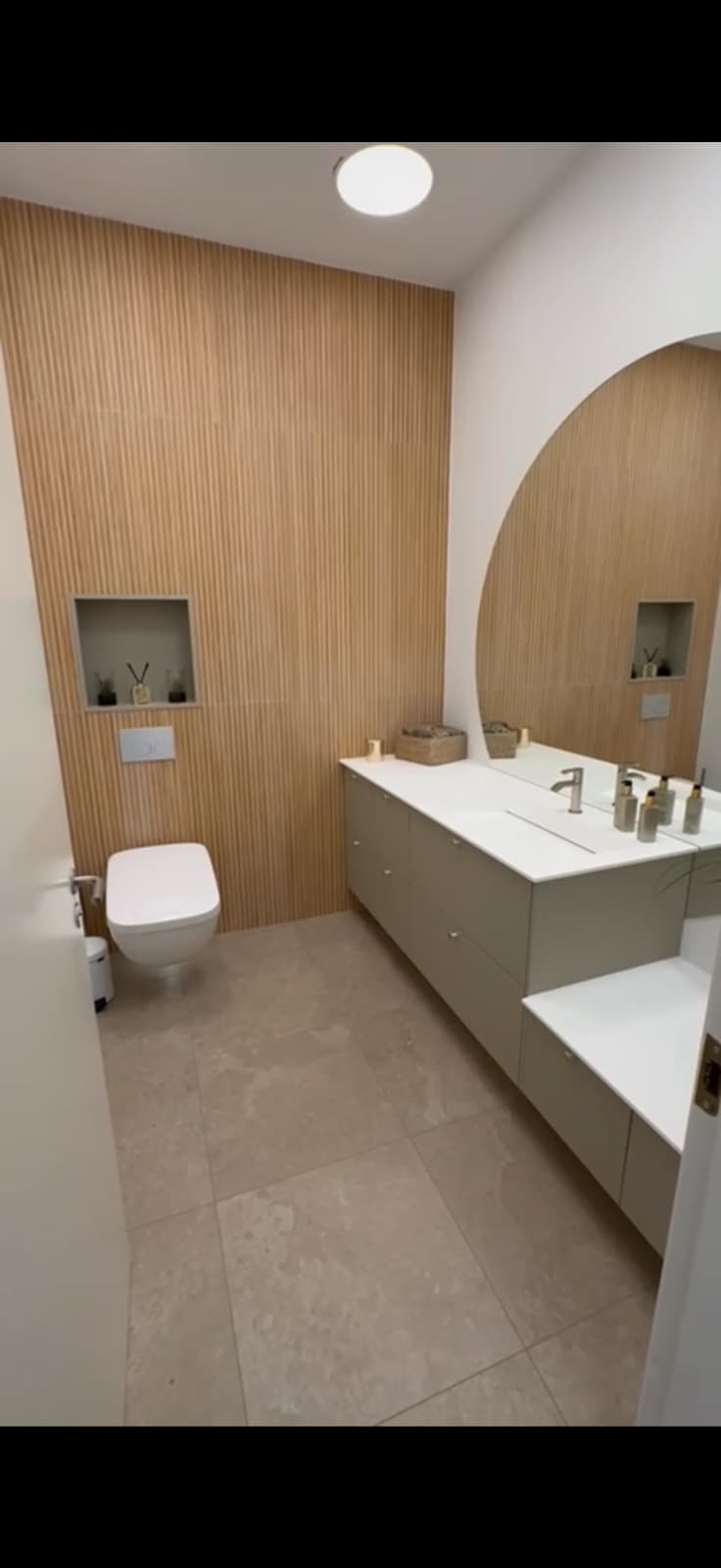 Gæstetoilet med træbeklædt væg og rundt spejl, udført af TMS-BYG